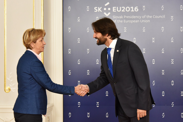 Bundeskanzlerin Angela Merkel und Bundeskanzler Joachim Gauck schütteln sich freundschaftlich die Hand vor einer Wand mit einem "EU-Gipfel"-Schild und einer Tür.
