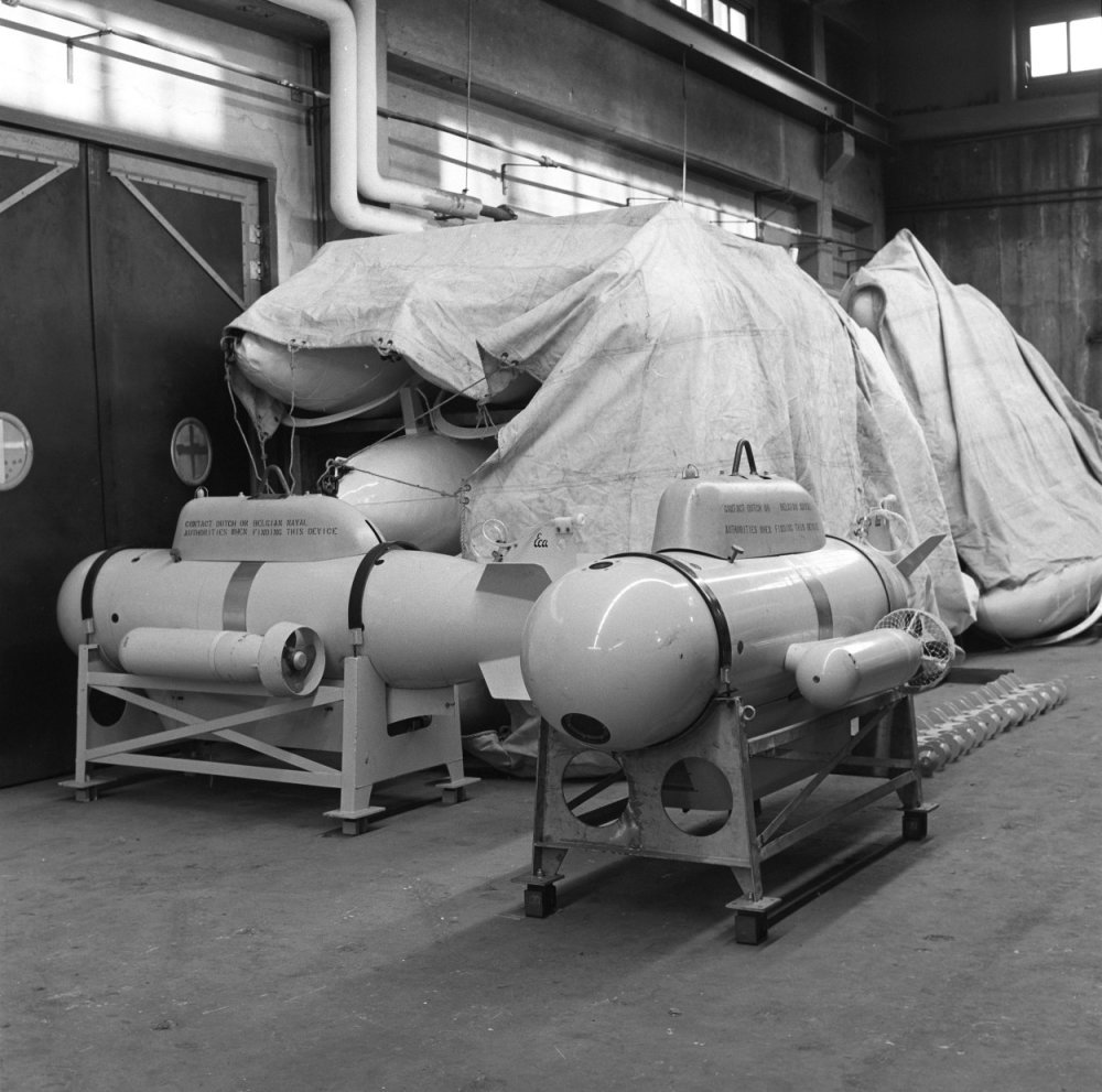 Ein Schwarz-Weiß-Foto eines Raums, der mit verschiedenen Tankarten gefüllt ist, darunter eine Wasserstoffbombe, mit einer Wand, einer Tür, Fenstern, Rohren und anderen Gegenständen im Hintergrund.