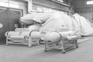 Ein Schwarz-Weiß-Foto eines Raums, der mit verschiedenen Tankarten gefüllt ist, darunter eine Wasserstoffbombe, mit einer Wand, einer Tür, Fenstern, Rohren und anderen Gegenständen im Hintergrund.