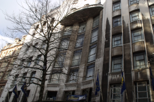 Gebäude mit Fenstern, einem Banner und Fahnen an den Polen unten und einem Baum mit Zweigen.