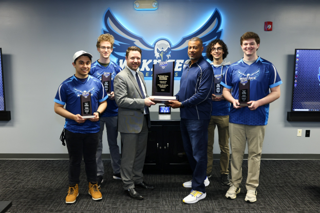 Gruppe von lachenden Männern mit Trophäen vor Fernsehern, die den Erfolg der Wake Tech Men's Basketball Mannschaft feiern.
