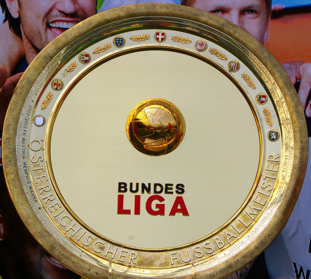 Goldener Schild mit "Bundesliga"-Text, gehalten von einem Mann, mit einem Banner mit drei Personen im Hintergrund.