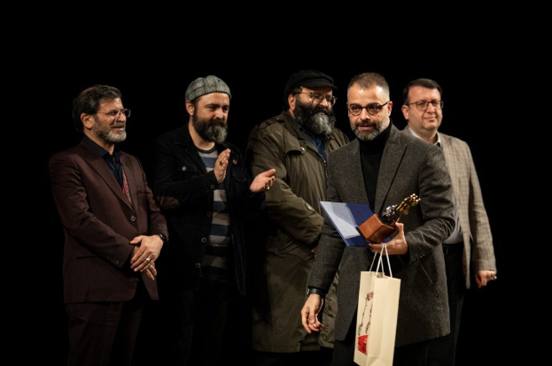 Eine Gruppe von Männern auf einer Bühne, einer hält eine Tasche und eine Trophäe, feiert die Eröffnungsnacht des Berliner Filmfestivals.