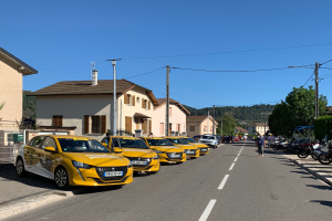 Eine Reihe gelber Taxis, die auf der Seite einer Straße geparkt sind, mit Menschen, die auf dem Gehweg rechts gehen, Gebäuden, Bäumen, Polen, Drähten und einem klaren blauen Himmel im Hintergrund.
