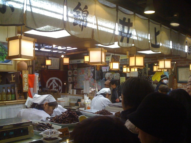 Restaurantmitarbeiter bereiten Essen hinter einer Theke mit Kunden davor zu, Sauceflaschen, Menükarten und Lampen sind im Hintergrund zu sehen.