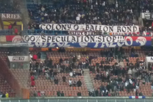 Ein Stadion voller großer Menge, Banner und Stühle, mit einem Zaun unten und Treppen auf der linken Seite.