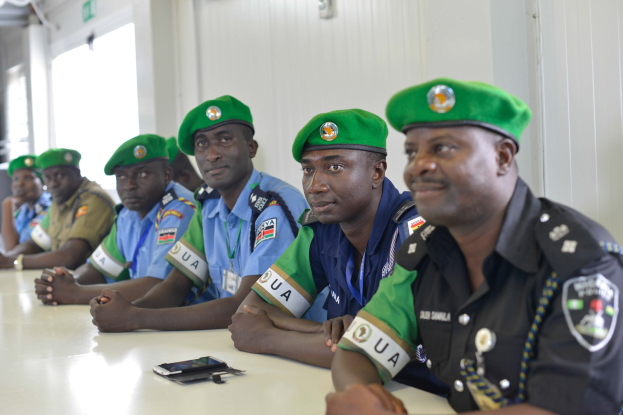 Gruppe von Polizisten bei einer Schulung an einem Tisch mit Mobiltelefonen und anderen Gegenständen in einem Raum mit Fenstern und Deckenbeleuchtung.
