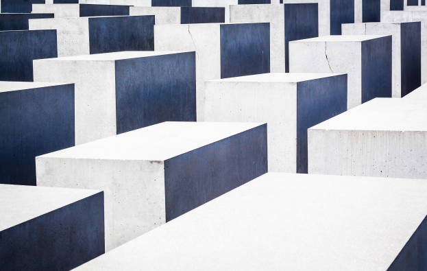 Luftaufnahme des Holocaust-Mahnmals für die ermordeten Juden Europas in Berlin, mit zahlreichen weißen und blauen rechteckigen Betonsteinen in einem Gittermuster.