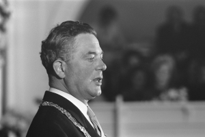 Ein Mann im Anzug und Krawatte steht an einem Podium mit einem Mikrofon und spricht zu einer unscharfen Menge, der ein Politiker zu sein scheint.