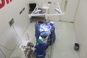 Chirurgen führen einen Eingriff an einem Patienten in einem Operationssaal durch, umgeben von medizinischer Ausrüstung, mit einem Monitor und anderen Geräten im Hintergrund.