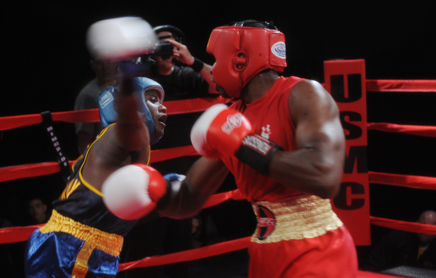 Zwei Boxer kämpfen in einem Boxring mit einem Fotografen und Zuschauern im Hintergrund bei dramatischer Beleuchtung.