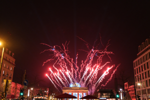 Ein festliches Silvesterfest in Berlin mit einer vollen Stadtstraße voller Menschen, Fahrzeuge und beleuchtete Gebäude, Feuerwerk erhellt den Himmel darüber.