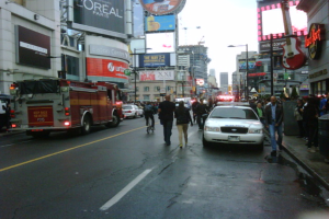 Eine belebte Straße mit parkenden Fahrzeugen auf beiden Seiten, Fußgänger auf der Straße und dem Gehweg sowie Geschäfte auf beiden Seiten.